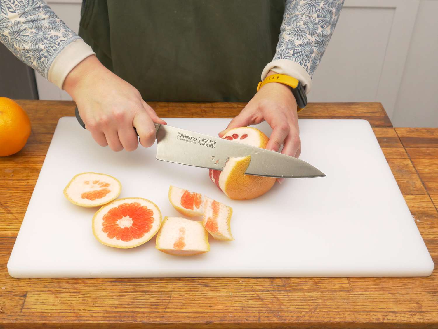 a person cutting the skin off of a grapefruit on the winco board