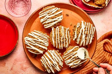 Gingerbread muffins with icing served on a plate with a hand applying more icing using a spoon