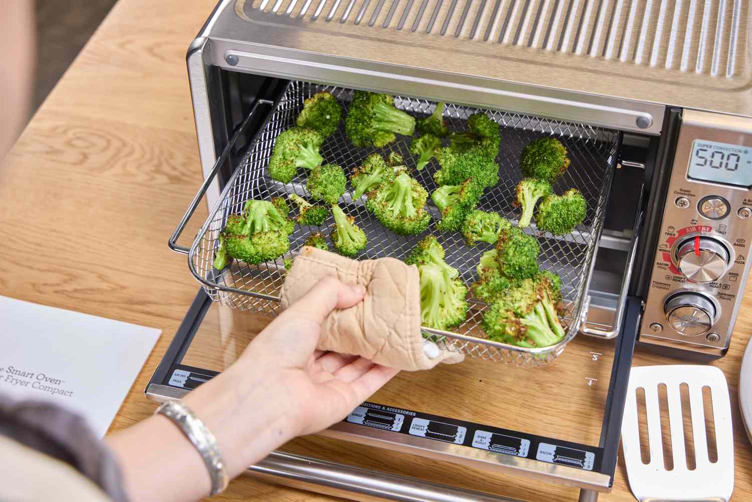 A person removes broccoli from the Breville The Smart Oven Air Fryer Compact