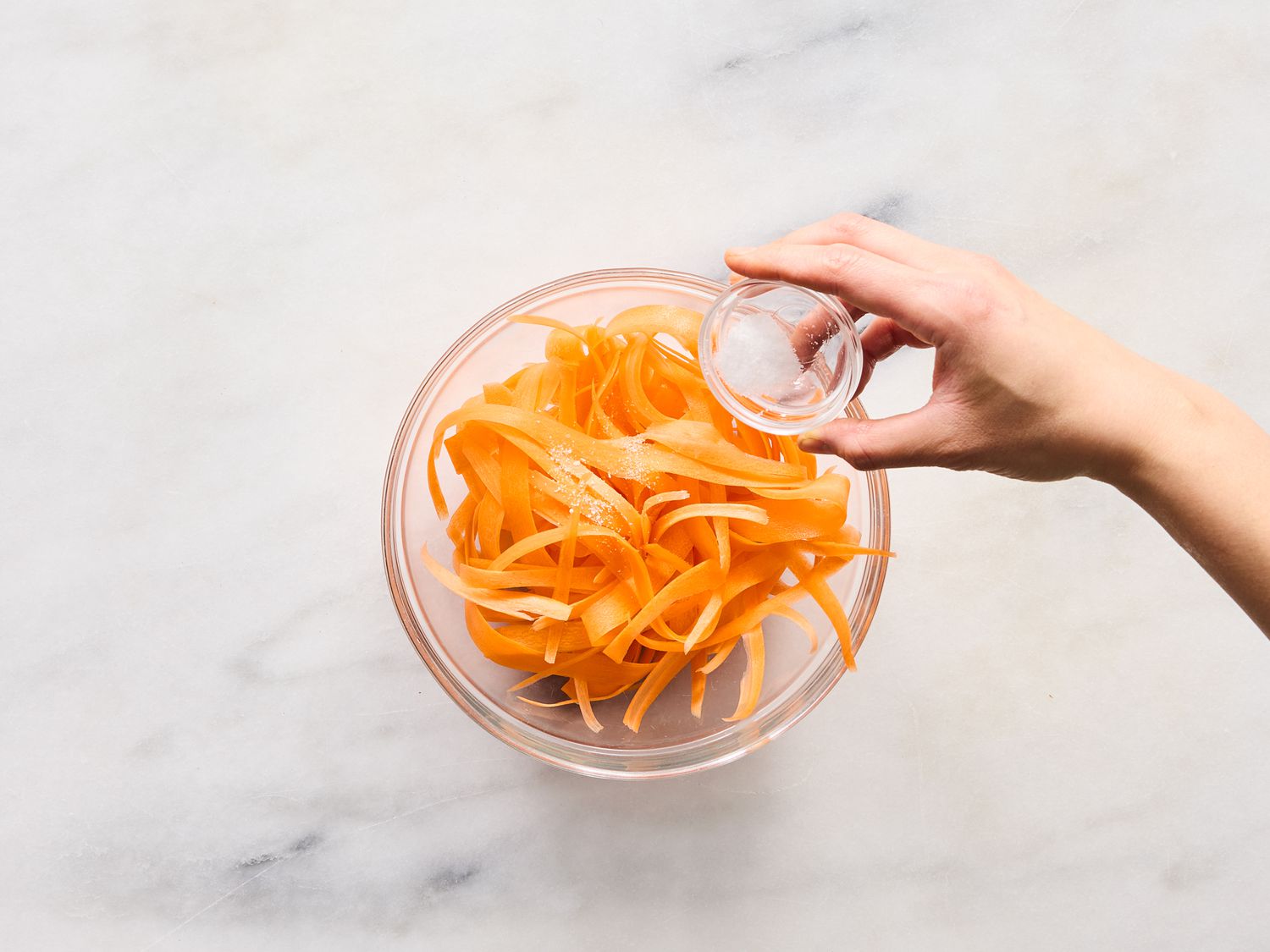 tossing carrot ribbons in a bowl with salt. 