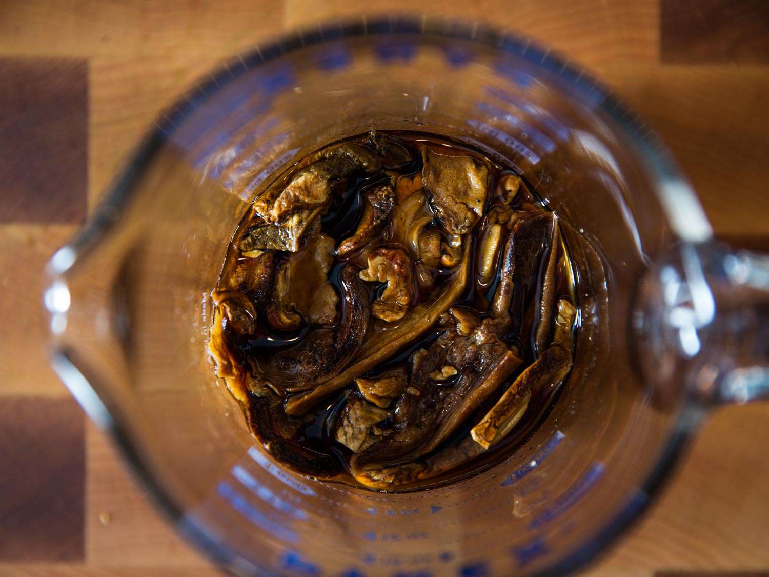 Overhead of dried mushrooms soaking in stock in a glass measuring cup.
