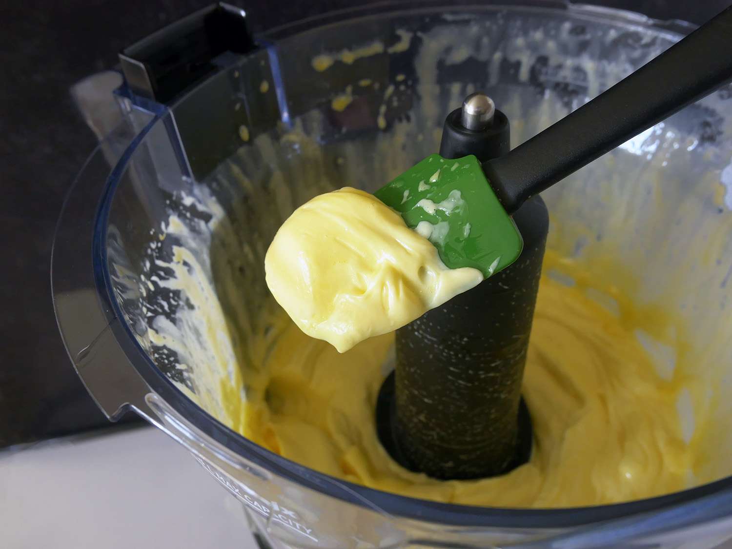 a closeup shot of a spatula scooping mayonnaise out of the vitamix food processor. 