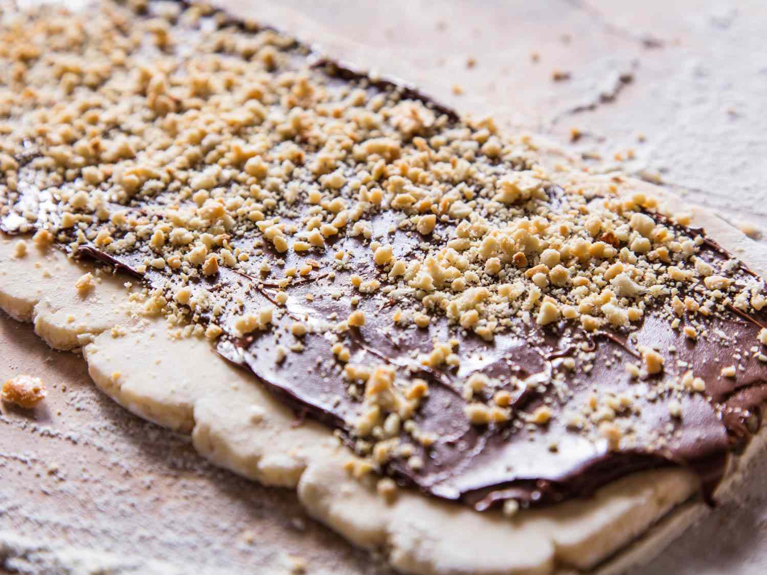 Rugelach dough rolled out on a work surface and covered with nutella and chopped peanuts.