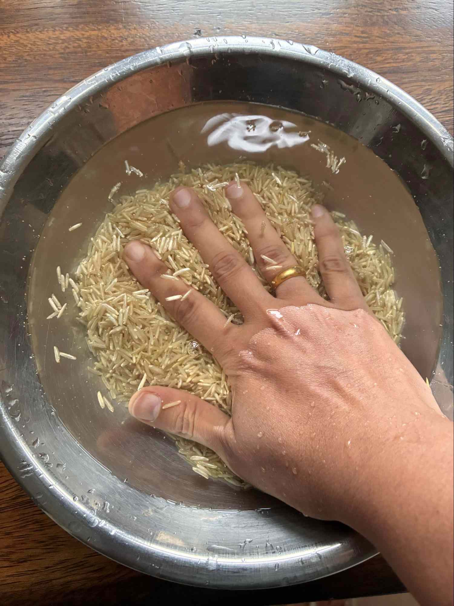 A hand washing rice in a bowl of water