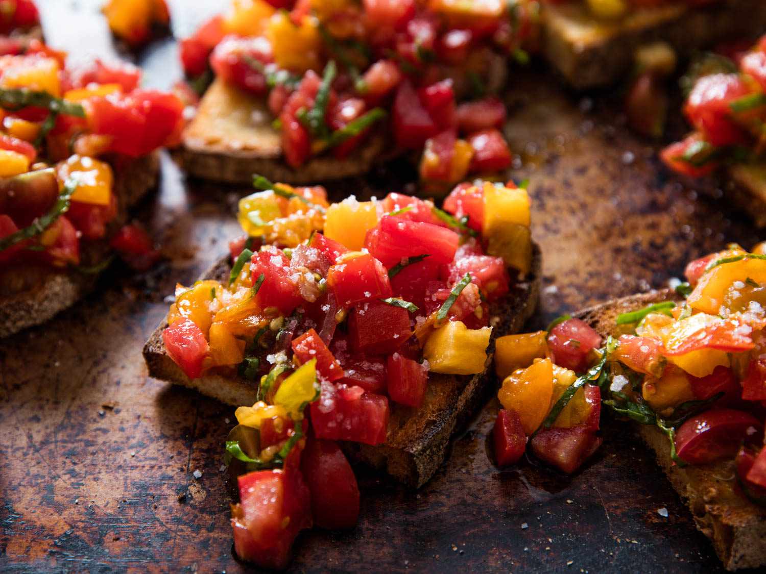 Glistening red and yellow tomato chunks with basil chiffonade on toast.
