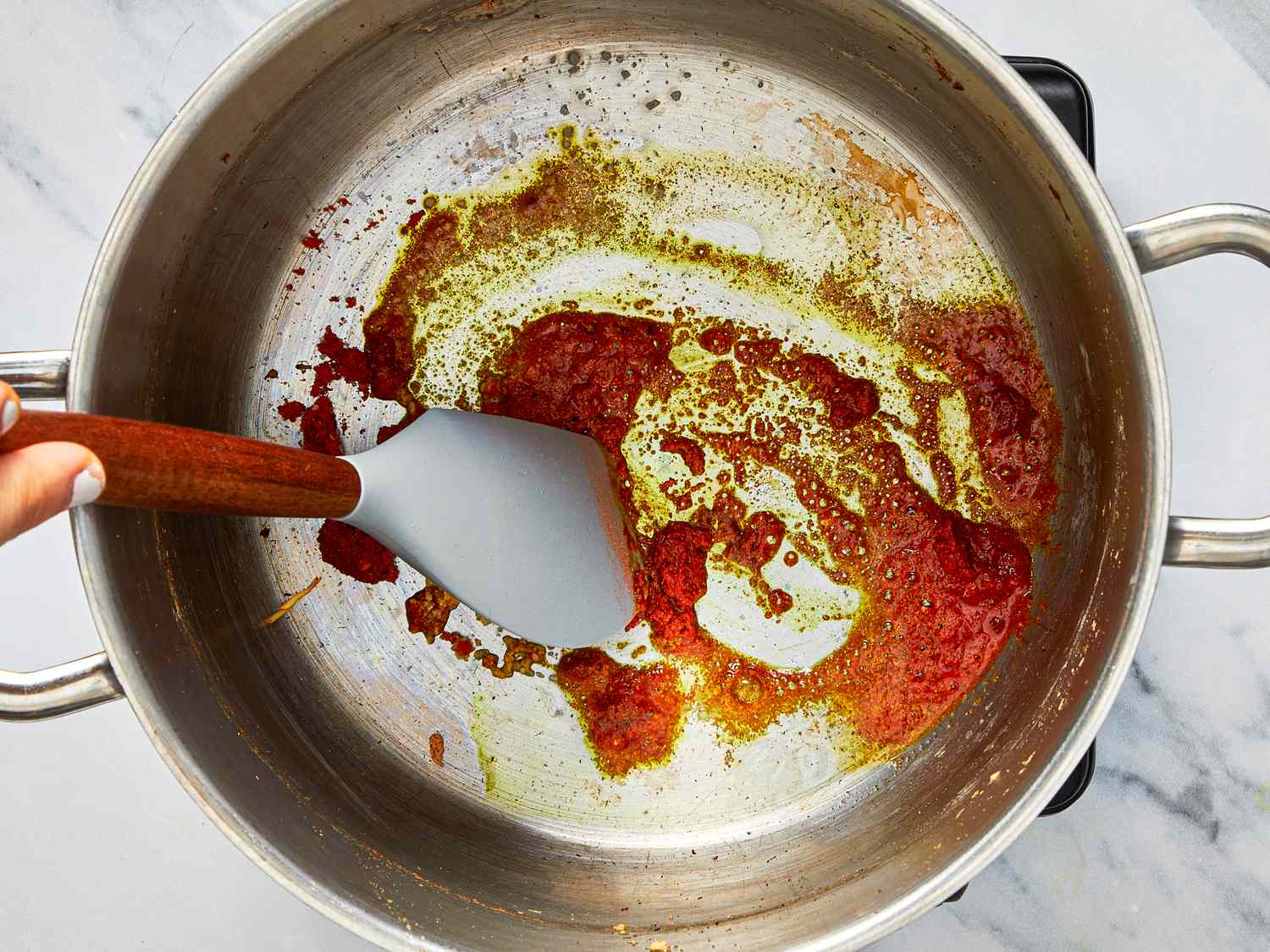 Cooking step showing a hand using a spatula to stir ingredients in a pot