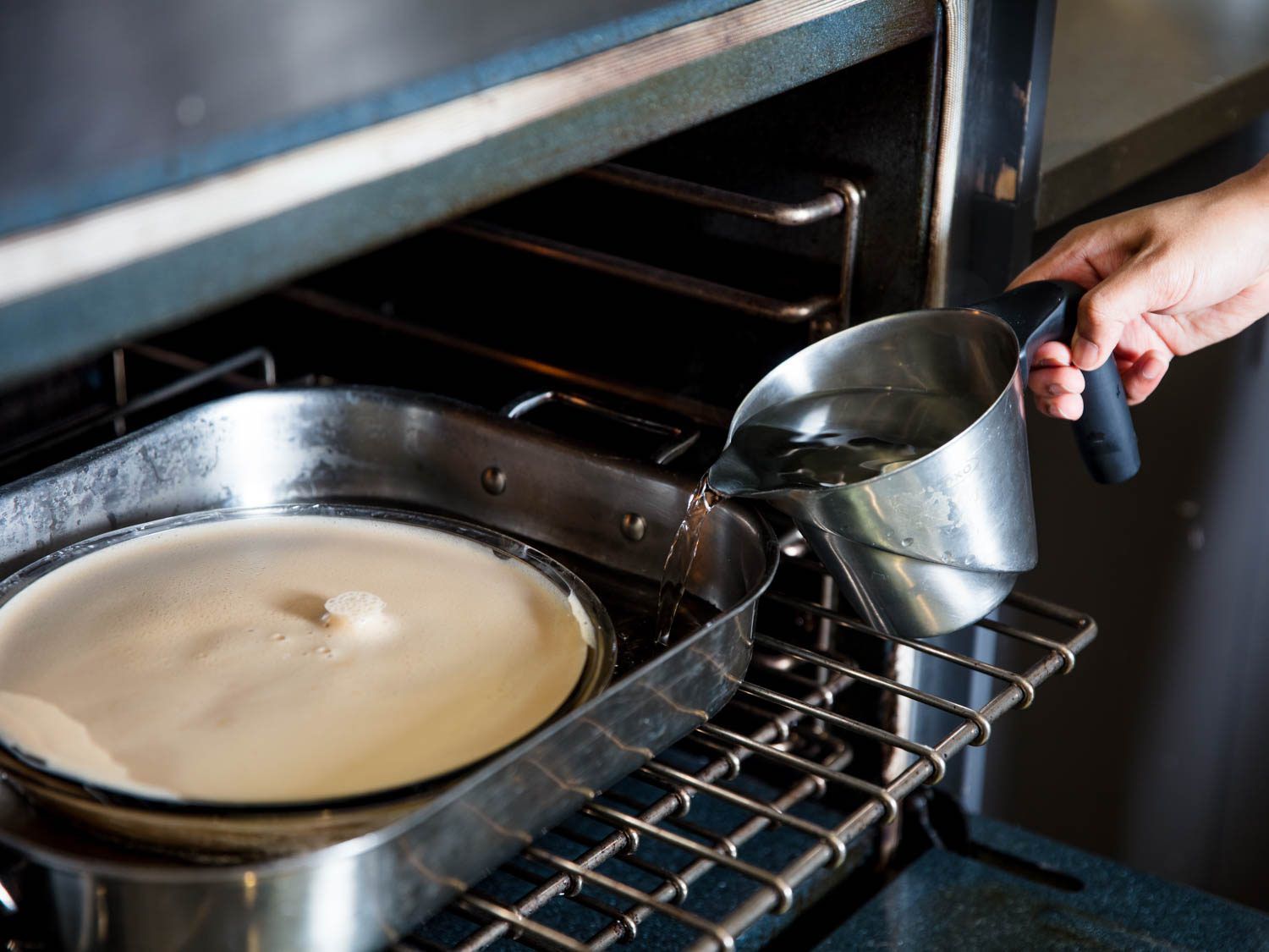 Filling a large baking pan with boiling water to gently cook the flan dish. 