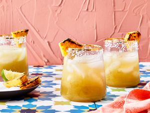 Three glasses of margarita with grilled pineapple garnishes on a colorful table