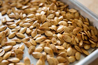 Closeup of roasted pumpkin seeds on a rimmed baking sheet.