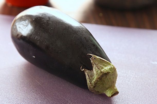 A whole purple eggplant resting on a cutting board.