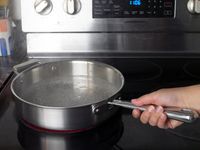a person holding the handle on a saute pan with boiling water