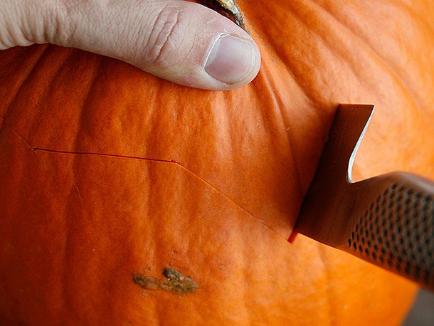 Cutting a jagged line around the top of a pumpkin with a chef's knife to make a lid