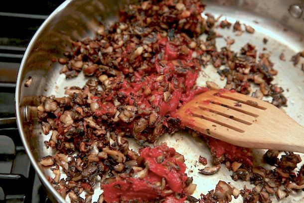 Tomato paste is stirred into the browned mushrooms.
