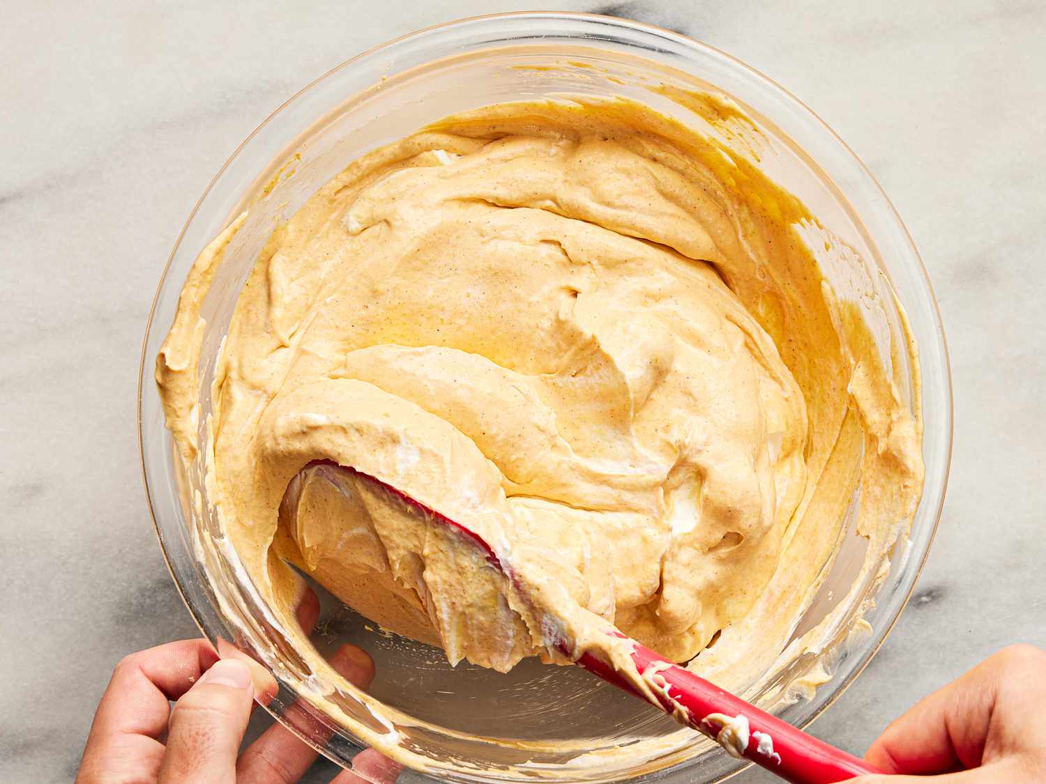 folding whipped cream into mascapone mixture in a glass bowl 
