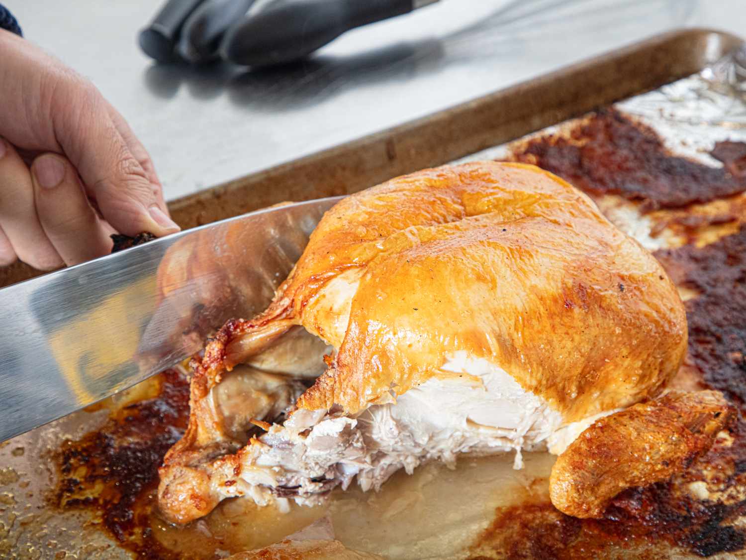 A person slicing a roasted chicken on a baking sheet using a knife
