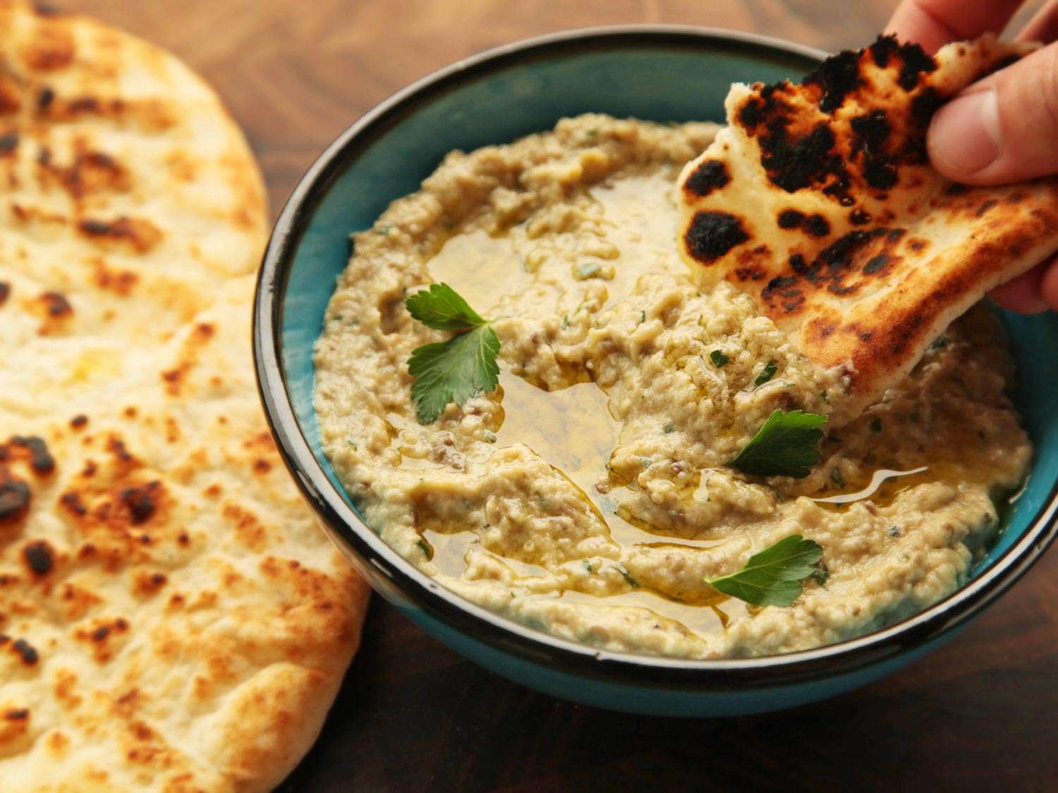 Dipping pita into a blue bowl of baba ganoush.