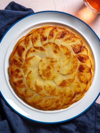A golden brown pommes anna sits on a serving plate, showing beautiful shingled rounds of thinly sliced potato.