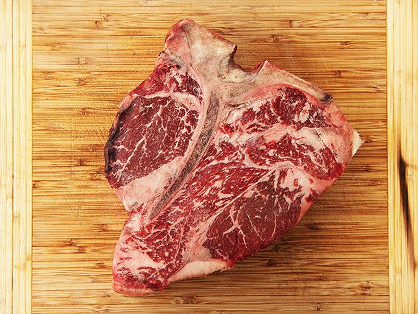Overhead shot of a well-marbled, dry-aged porterhouse steak sitting on a cutting board.