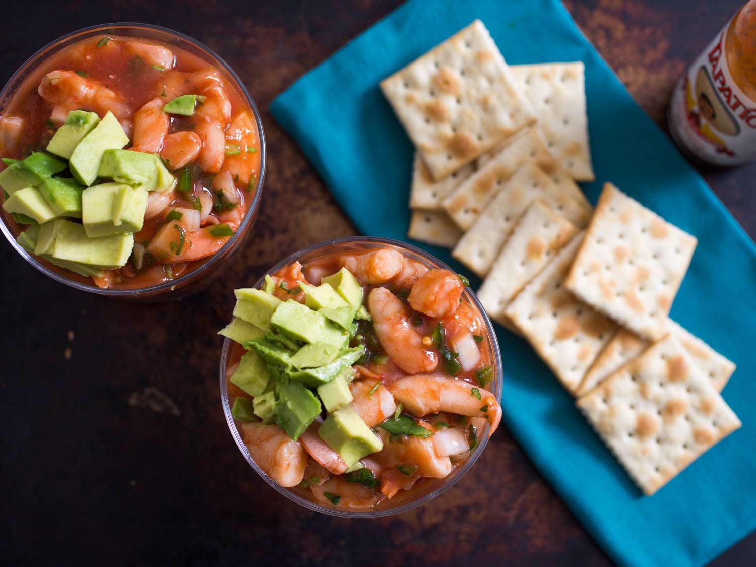 Overhead shot of two servings of Mexican shrimp cocktail with diced avocado and cilantro, with saltines on the side