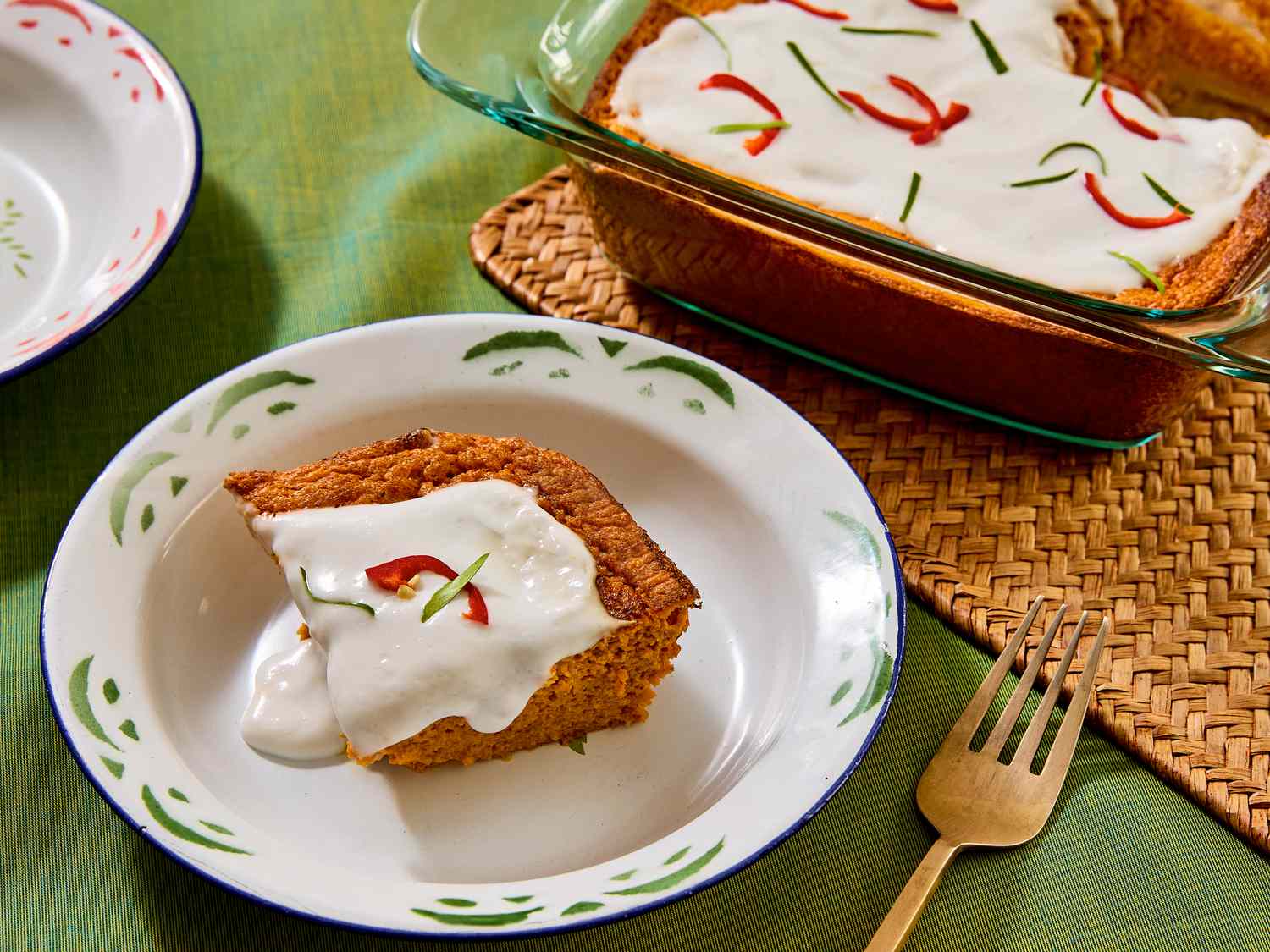 square of squash souffle in a white dish, and glass baking pan of whole souffle on a green fabric surface and rattan heat pad