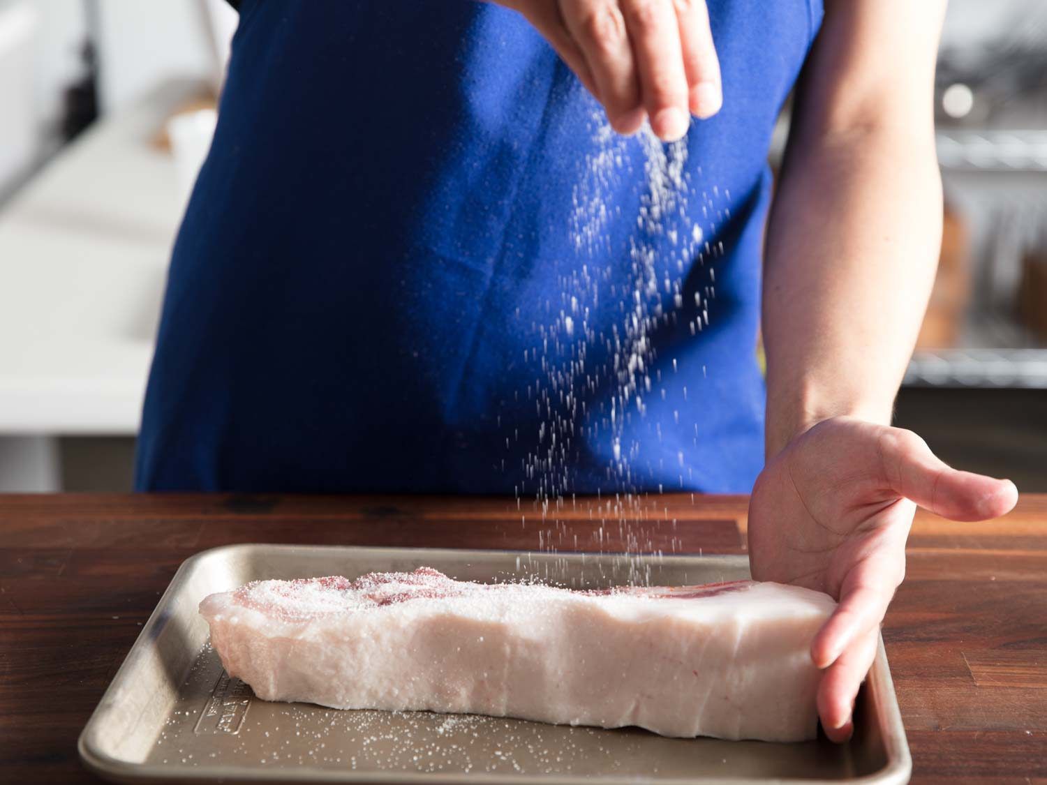 A slab of trimmed pork belly is sprinkled with salt.
