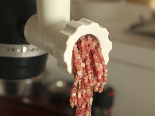 Front view of ground pork extruded from grinder attached to stand mixer