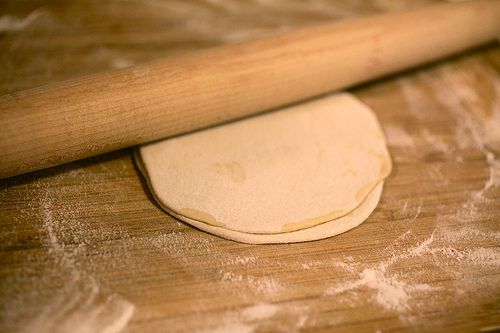 Thin pancakes on a well-floured wooden cutting board, with a tapered rolling pin on top of them.