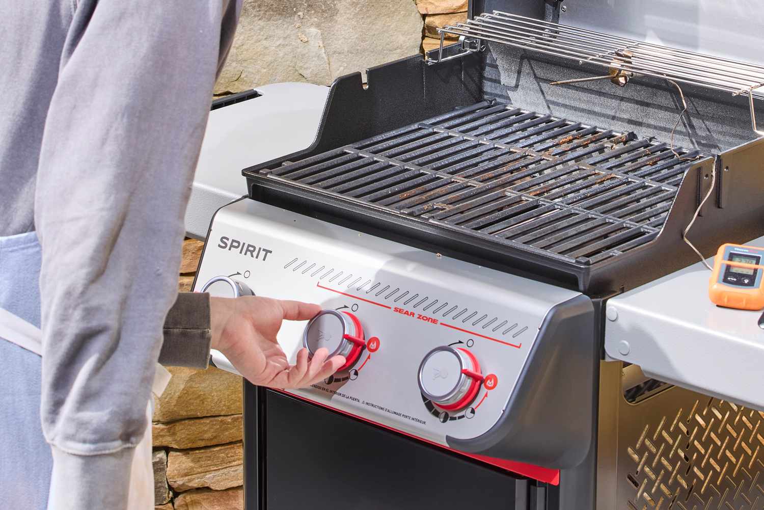 A close-up of a person turning the middle nob on the Weber Spirit E-325 Gas Grill