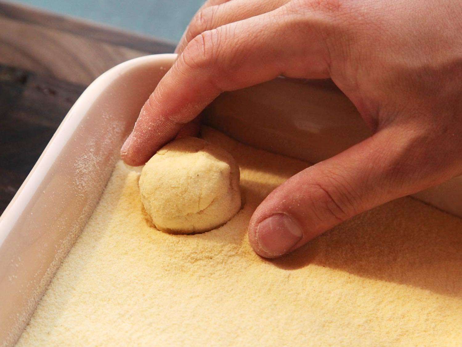 Dropping the semolina-coated ricotta mixture into a baking dish filled with more semolina. 