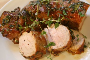 Closeup of honey-thyme roasted pork loin, served on a plate with a garnish of thyme sprigs.