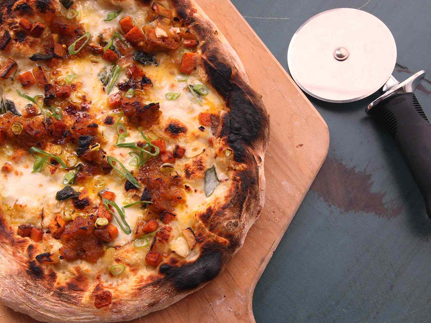 The finished pumpkin pizza on a wooden peel, ready to slice and serve. The edges of the crust are nicely charred.