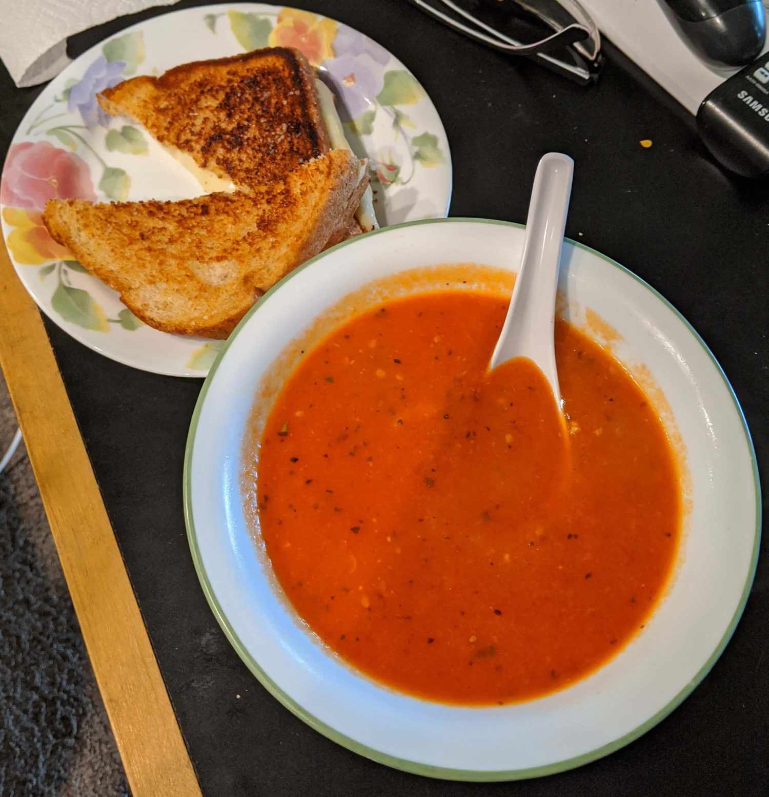 Bowl of tomato soup with a grilled cheese on a plate alongside