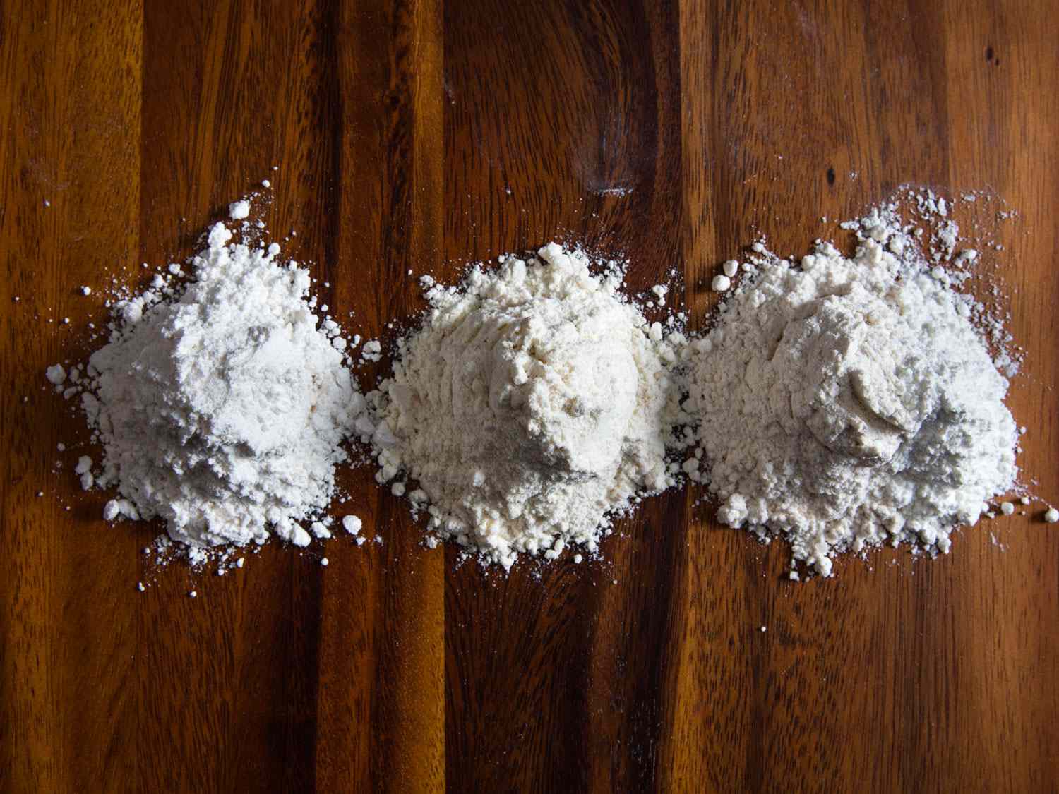 Three small piles of flour on a wooden surface