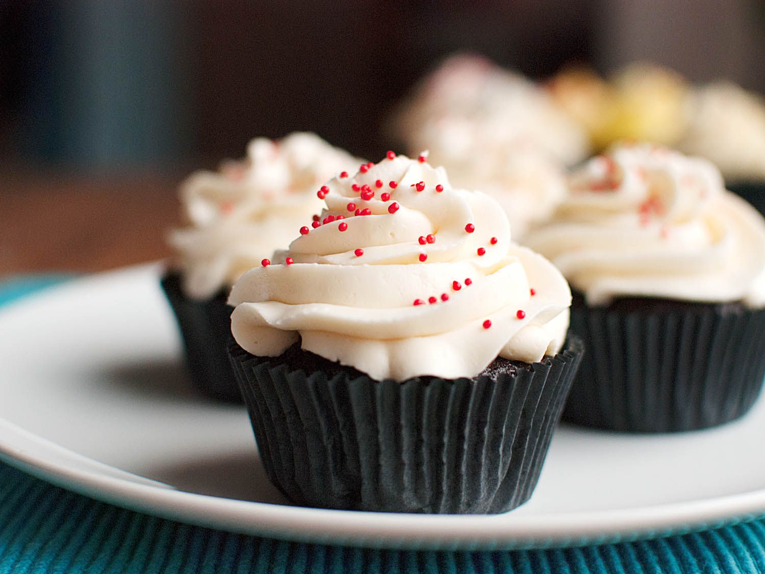 Three Swiss buttercream cupcakes with red sprinkles on top. 