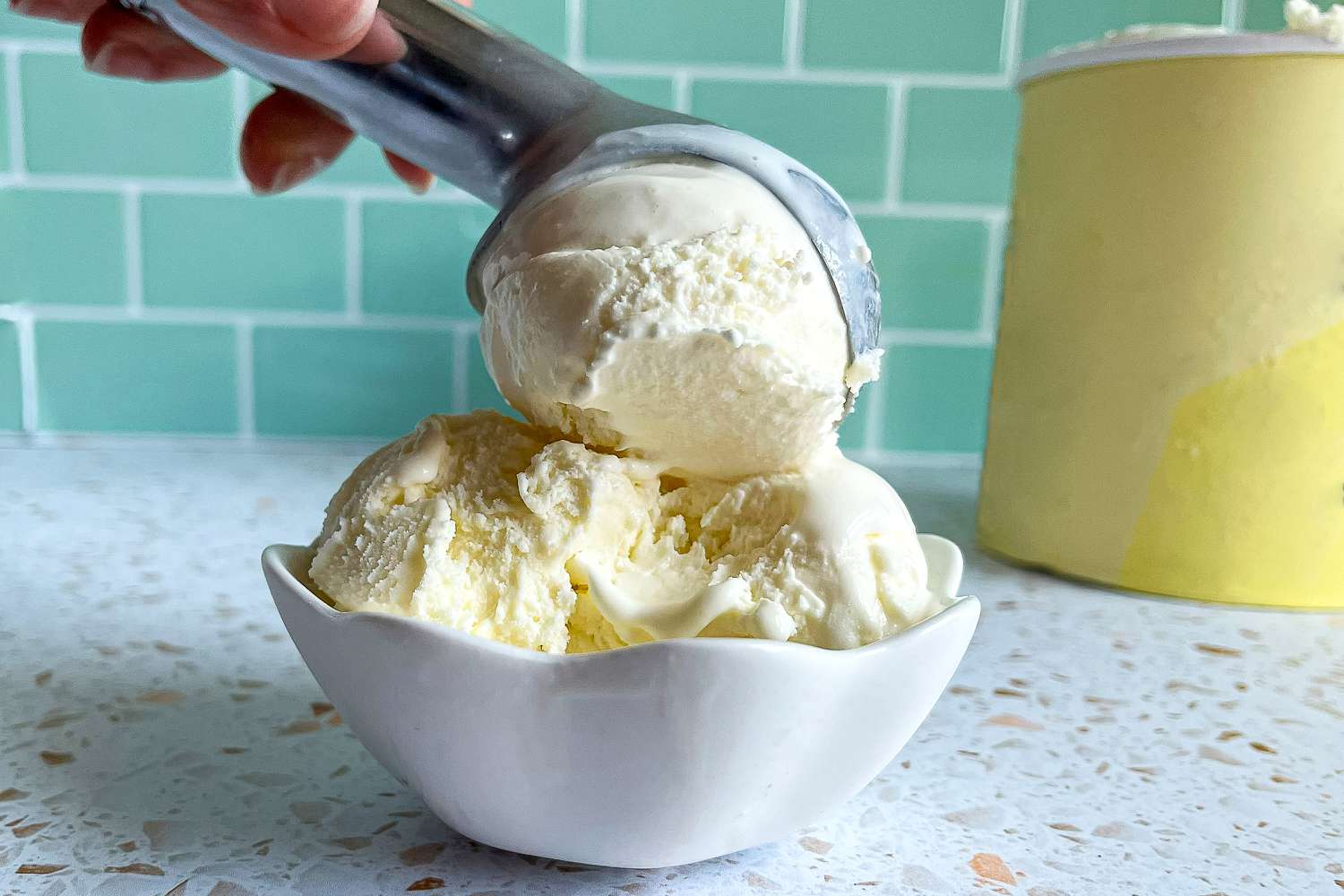 a person scooping vanilla ice cream into a bowl