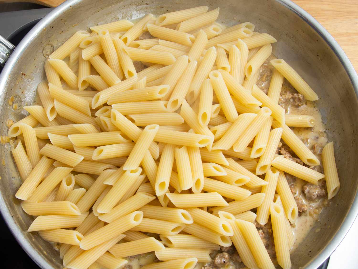Cooked penne pasta being cooked on top of sausage mixture in a large skillet.