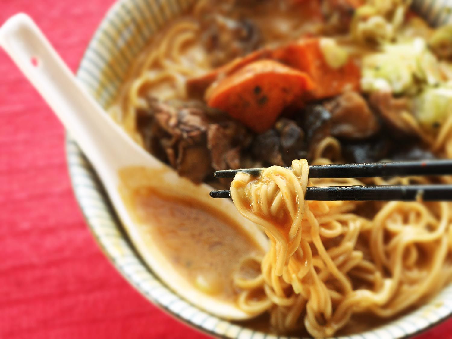 Chopsticks holding ramen noodles pulled from a bowl of creamy vegan ramen.