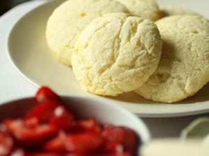 Closeup of gluten free short cakes on a plate. A bowl of strawberries is in the foreground, blurred by the narrow depth of field.