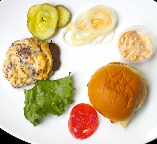 Overhead view of the components of a cheese burger from Shake Shack, disassembled and laid out on a white platter.