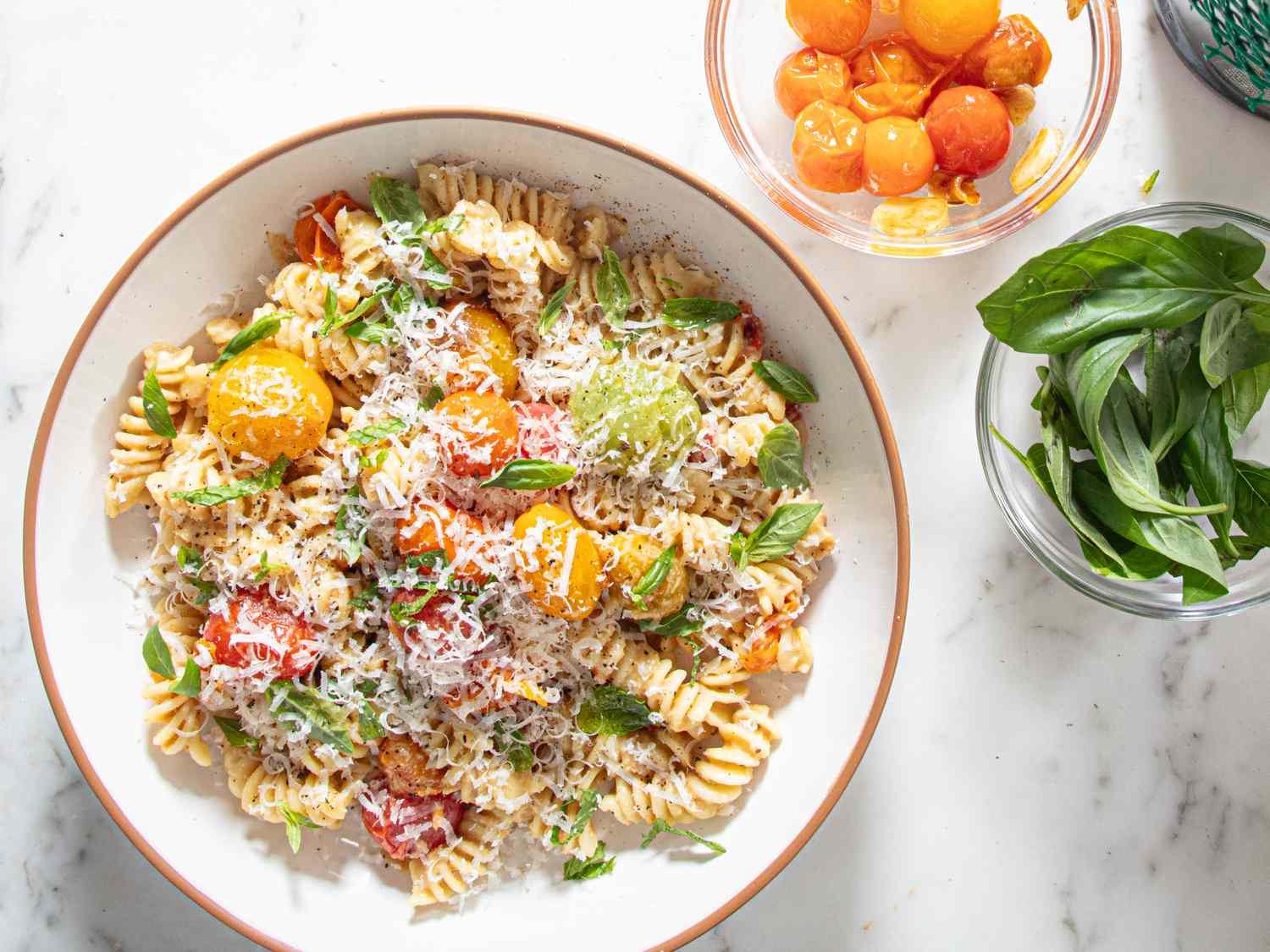 Fusilli pasta served with roasted cherry tomatoes grated cheese and fresh herbs accompanied by bowls of additional ingredients