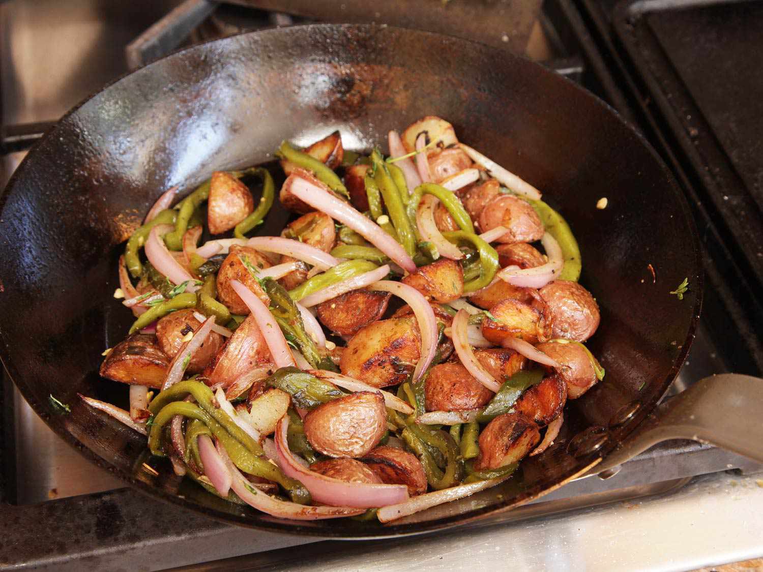 Saute pan filled with strips of green poblano pepper, red onion, and chunks of golden brown potato