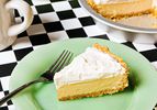 A slice of creamtopped pie on a green plate with a fork a pie plate with the rest of the pie in the background