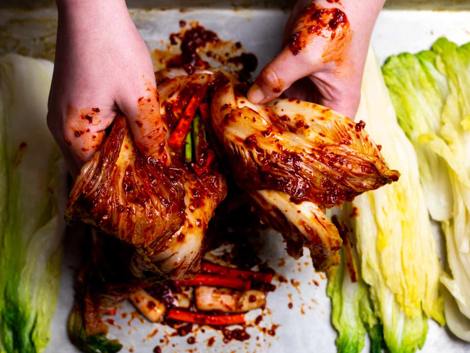 hands rubbing vegetable/gochugaru mixture into all of the cabbage leaves