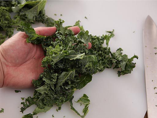 Author clutching a handful of kale cut into bite-sized pieces over a cutting board.