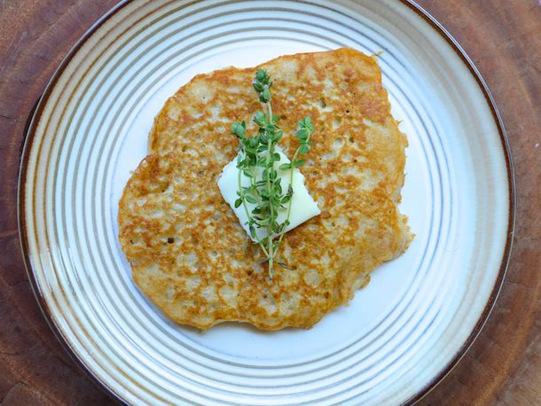 Overhead view of an oatcake, topped with apat of butter and a sprig of fresh thyme.