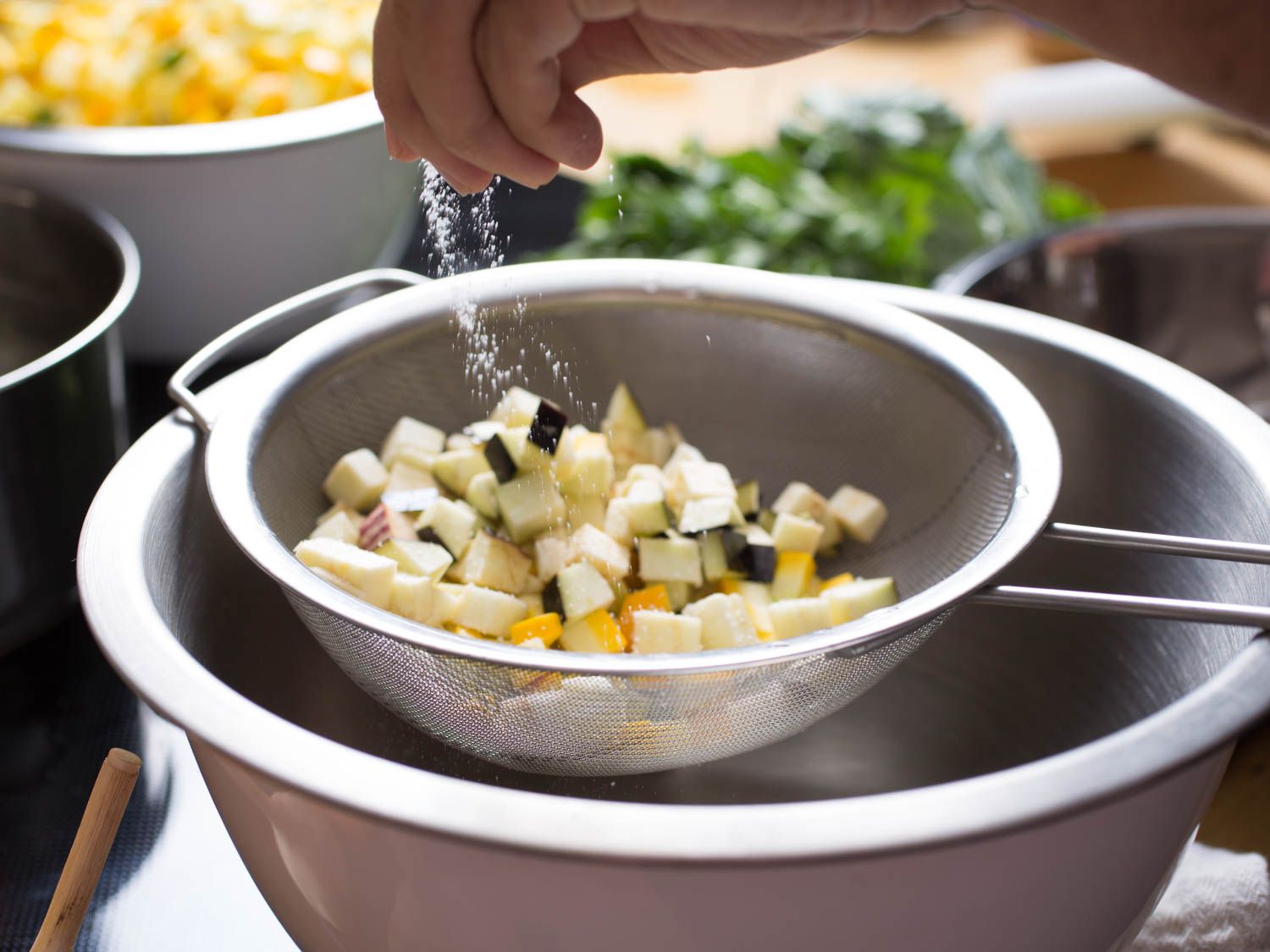 Author sprinkling salt over a fine mesh strainer containing diced summer squash.