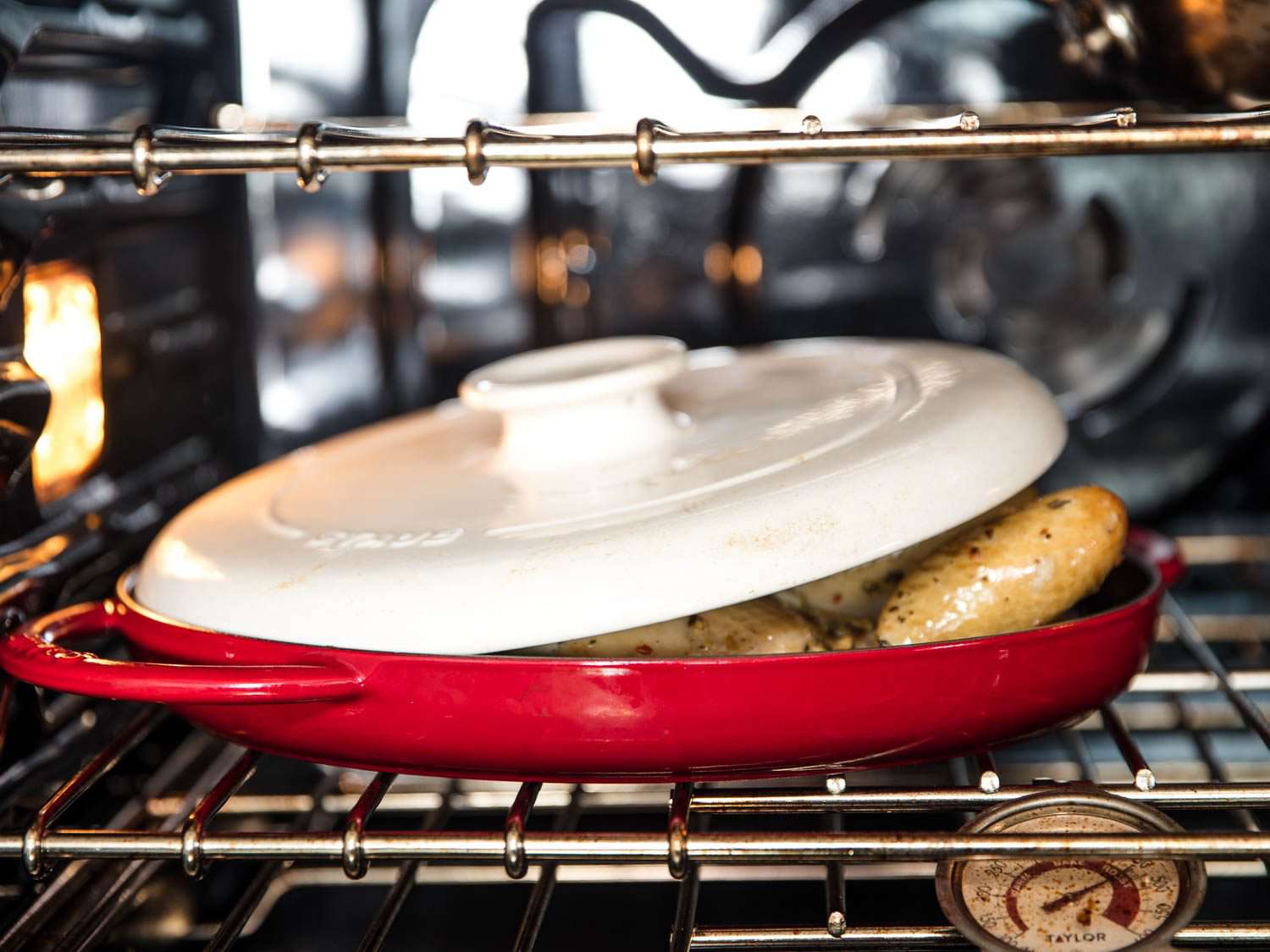 A white ceramic mattone sitting on a spatchcocked roast chicken in a red pan.