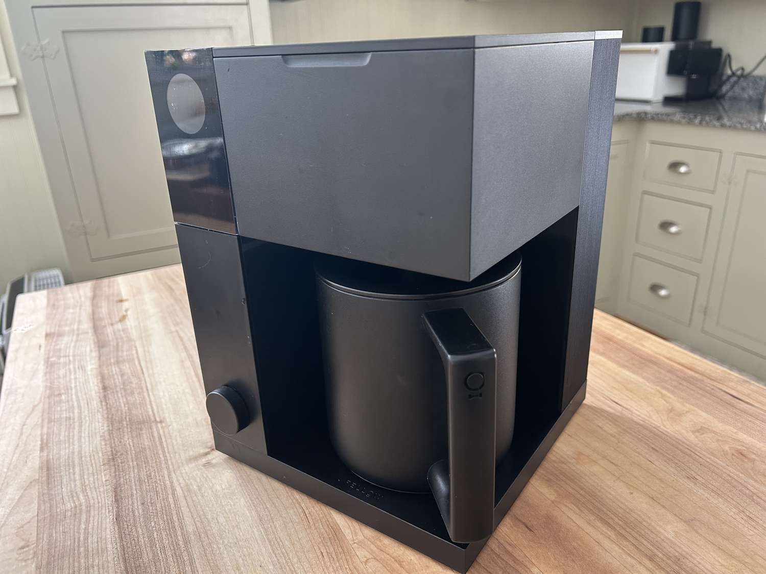 The Fellow Aiden coffee maker on a wooden table in a kitchen.