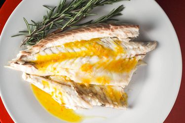 An overhead view of a piece of branzino drizzled with citrus vinaigrette on a while plate next to sprigs of fresh rosemary.