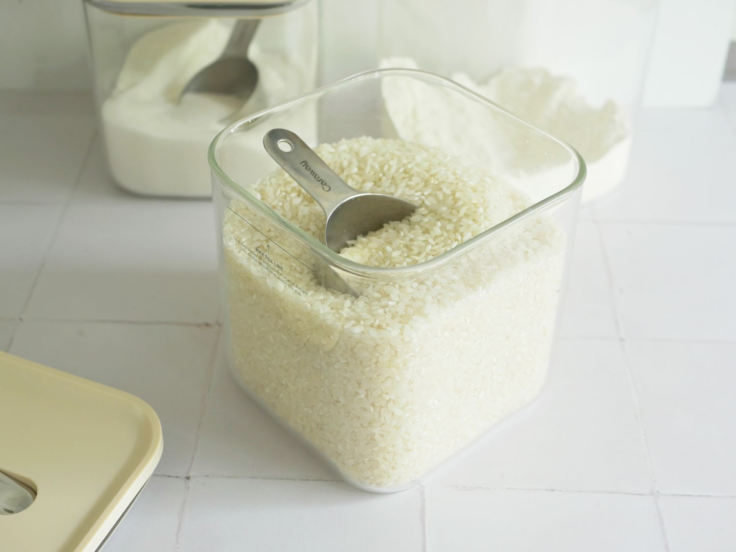 The caraway glass storage container with the lid off and a scoop in the rice inside